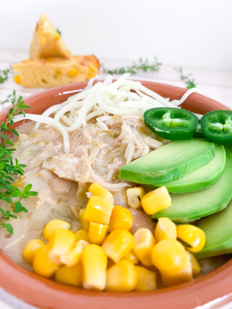 Instant Pot White Chicken Chili topped with shredded cheese, thyme, jalapenos, avocado and corn