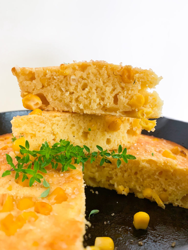 two slices of cornbread stacked up on the wheel of small batch corn bread in a cast iron with a sprig of thyme