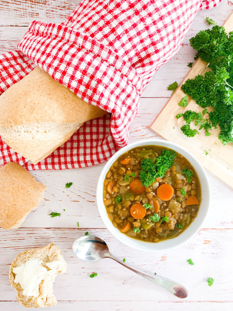 Overhead of french lentil soup in a small bowl with chopped parsley and a loaf of bread