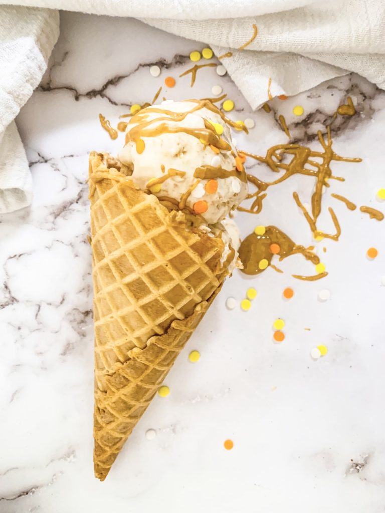 melting peanut butter swirl ice cream cone with extra peanut butter drizzle and orange and yellow sprinkles