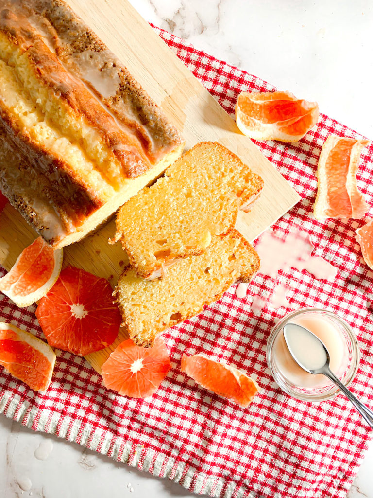 two slices of grapefruit pound cake on a cutting board with a small bowl of icing.
