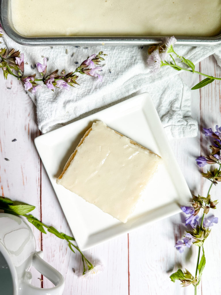 Brown Butter Vanilla Texas Sheet Cake slice on a square plate with sage blossoms